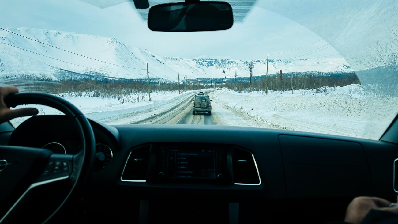 View from inside a car following another SUV on a snow-lined road through the snowy Kola Peninsula mountains.
