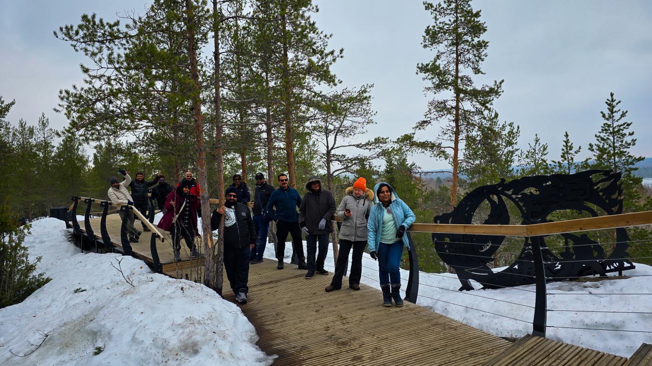 A group of tour participants walking along a snowy boardwalk through a pine forest in the Russian Arctic.