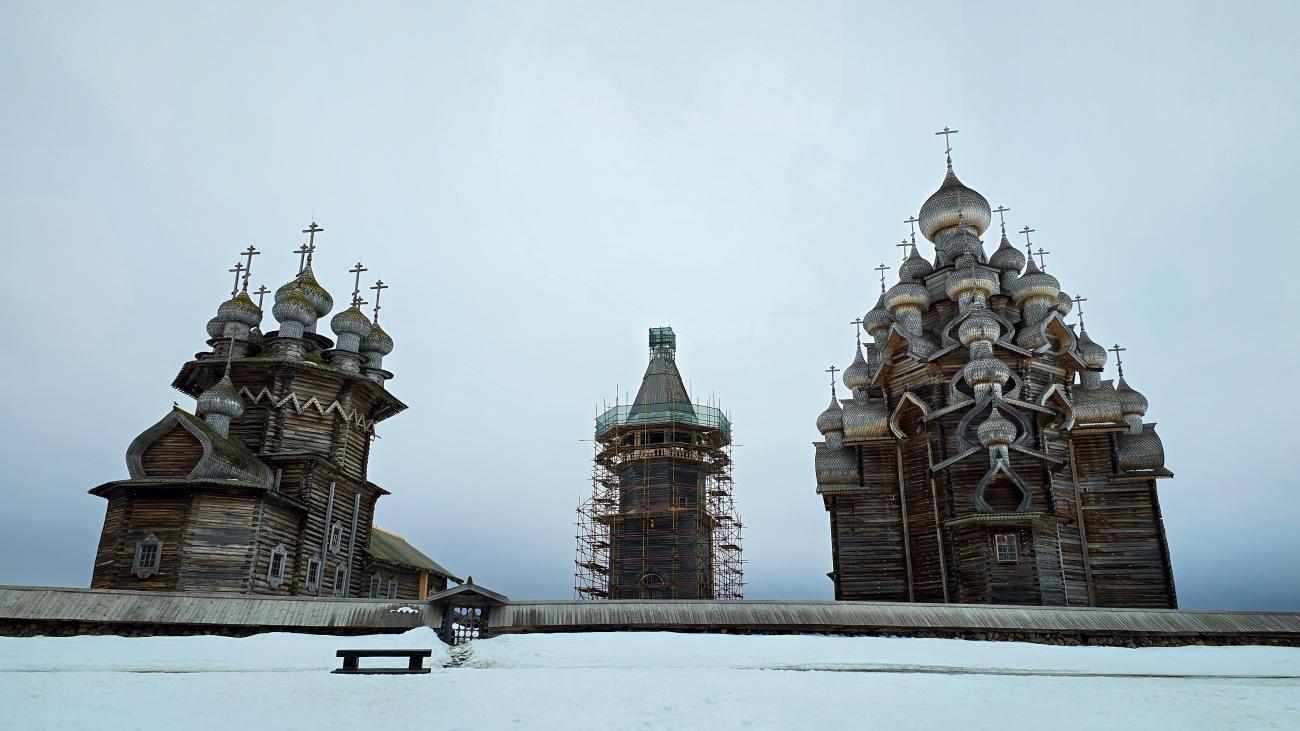 The historic multi-domed wooden churches of Kizhi Pogost standing against an overcast winter sky with snow on the ground.