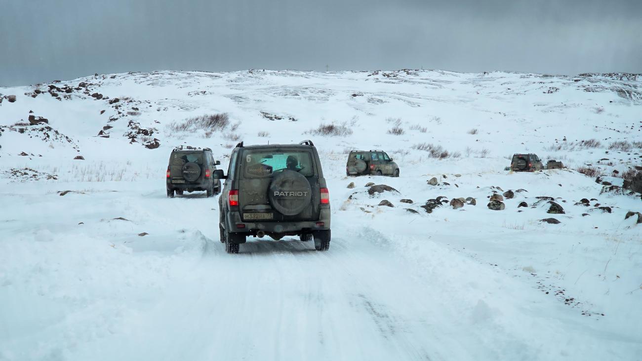 UAZ Patriot SUVs driving in convoy along a snowy off-road trail through the barren Arctic hills.