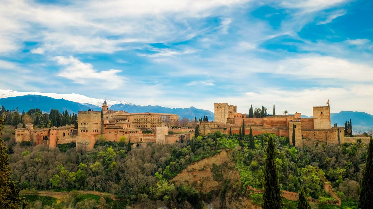 Panoramic view of the Alhambra palace complex in Granada with snow-capped Sierra Nevada mountains behind.