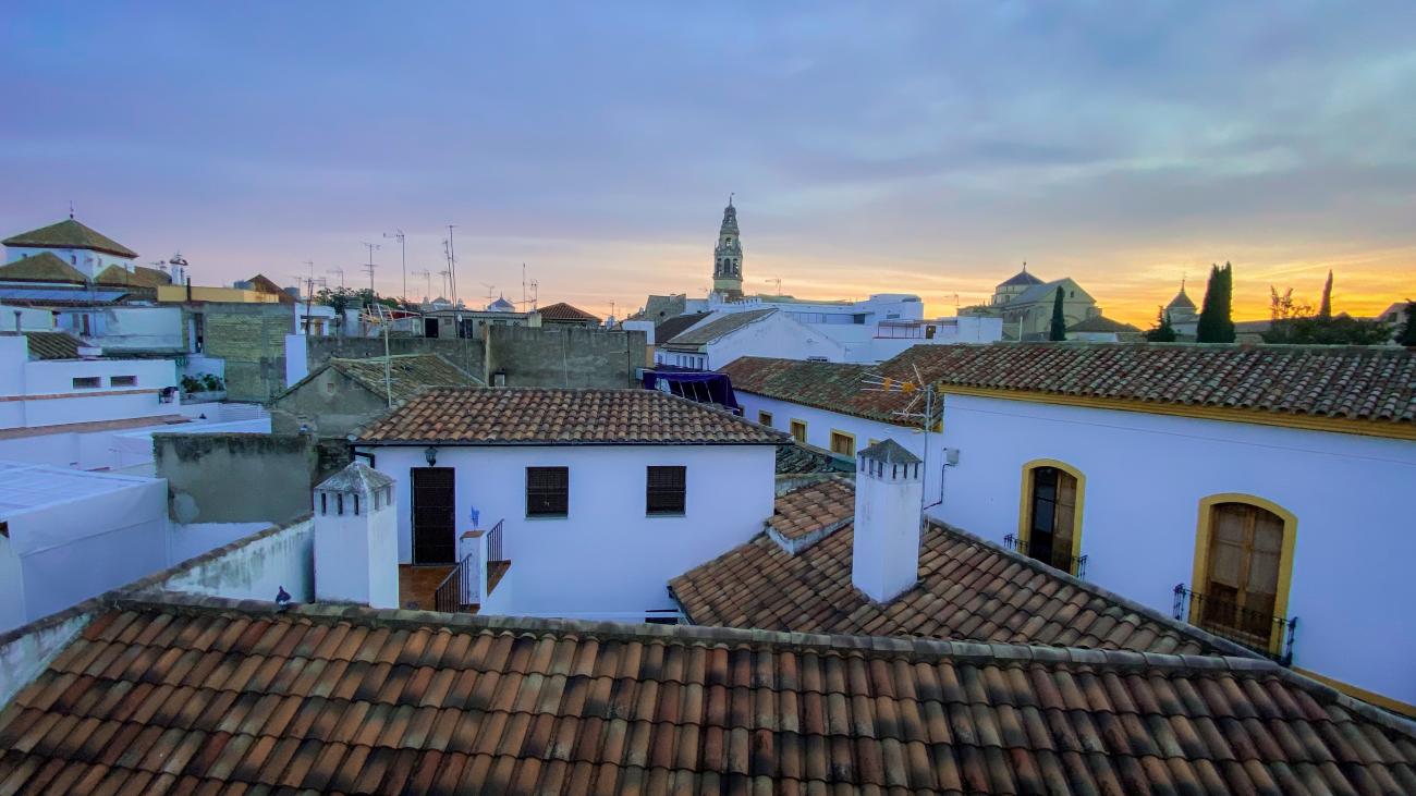 Sunset view across the terracotta rooftops of Cordoba with the Mezquita bell tower in the distance.
