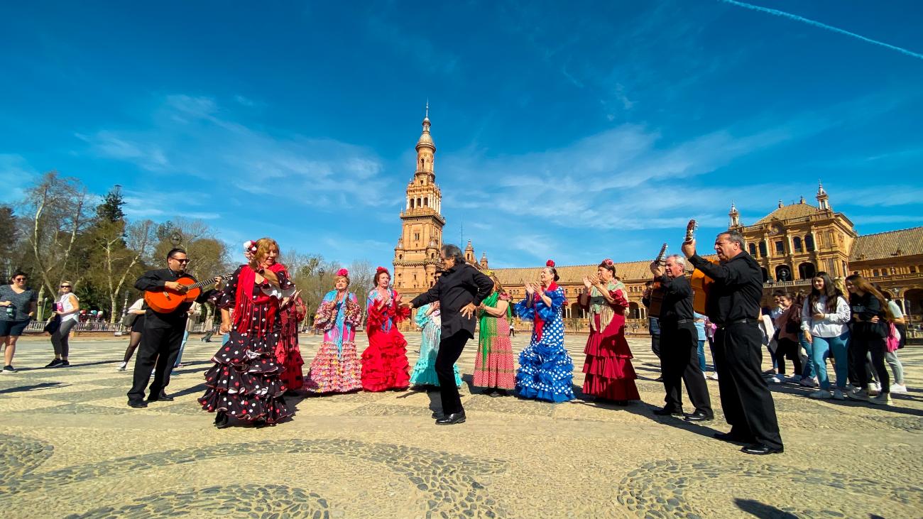 Flamenco dancers in colorful traditional dresses performing with guitarists at Plaza de Espana in Seville.