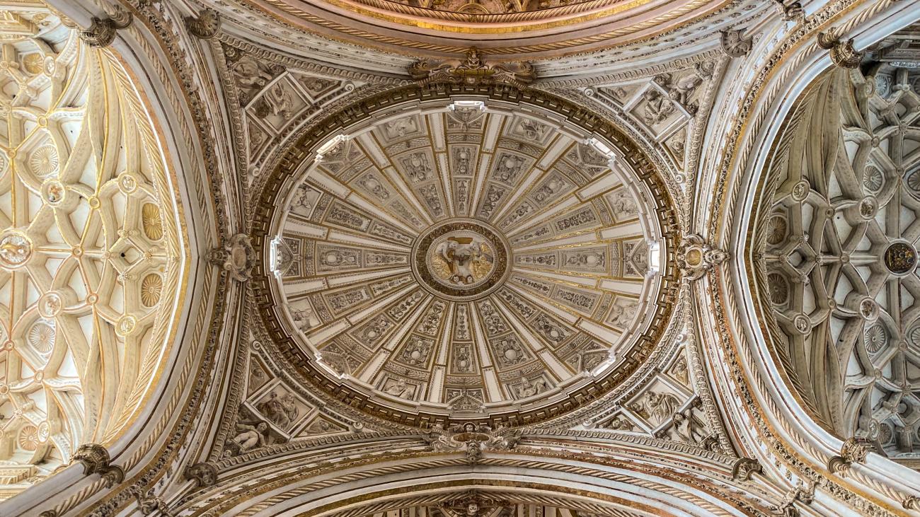 Ornate Renaissance dome ceiling inside the Mezquita-Cathedral of Cordoba with intricate carved stone details.