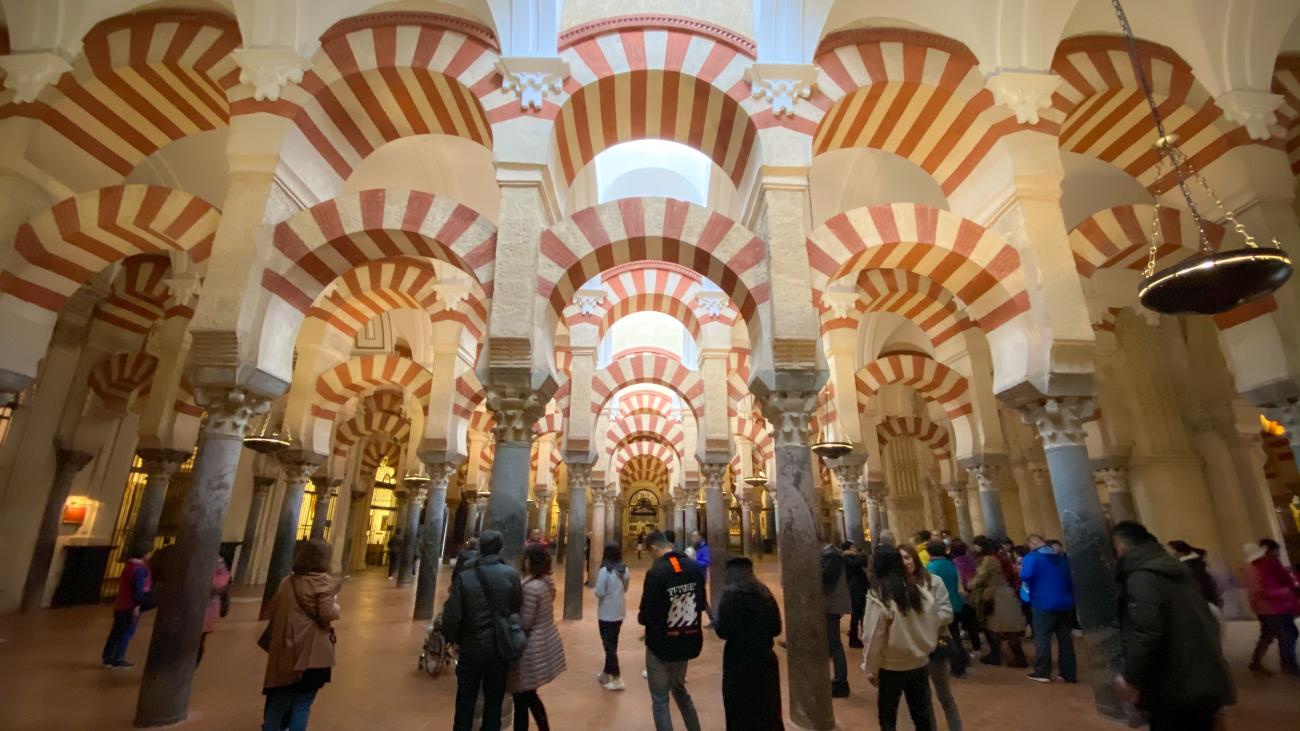 Visitors walking beneath the red-and-white striped double arches inside the Mezquita-Cathedral of Cordoba.