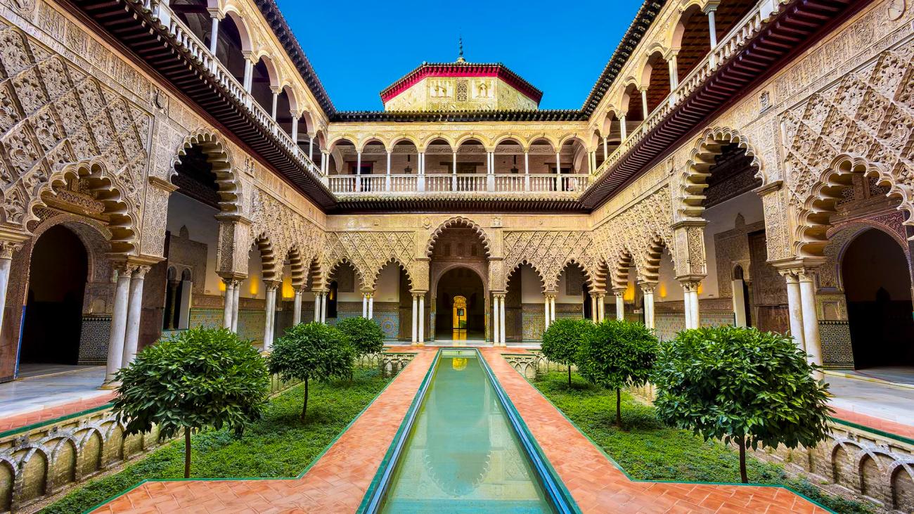 Ornate Mudejar courtyard with reflecting pool and manicured gardens inside the Real Alcazar of Seville.