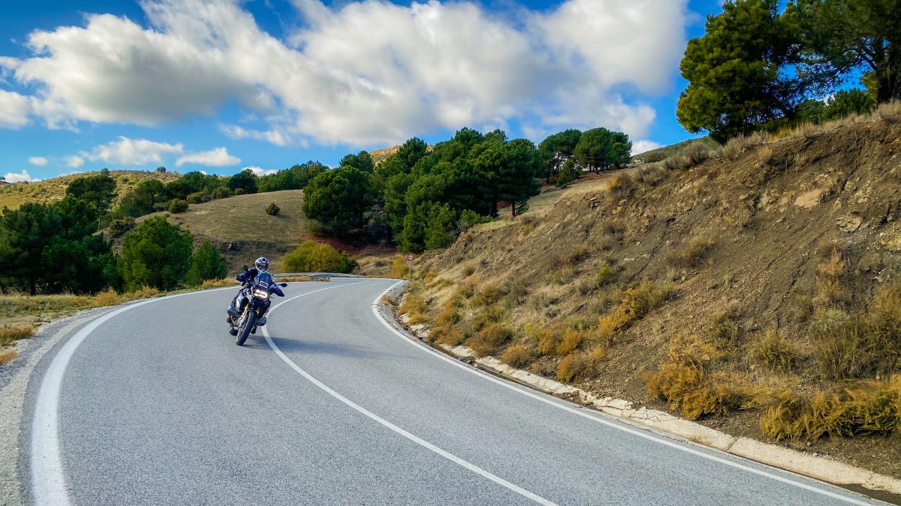 Motorcyclist leaning into a curve on a scenic mountain road through the rolling hills of Andalucia.