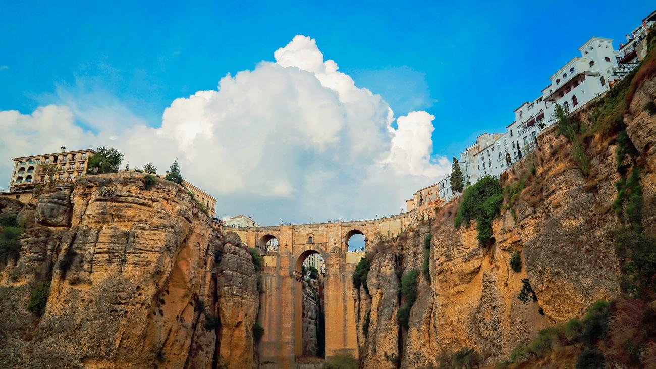 The iconic Puente Nuevo bridge spanning the El Tajo gorge in Ronda, Andalucia, with dramatic clouds above.