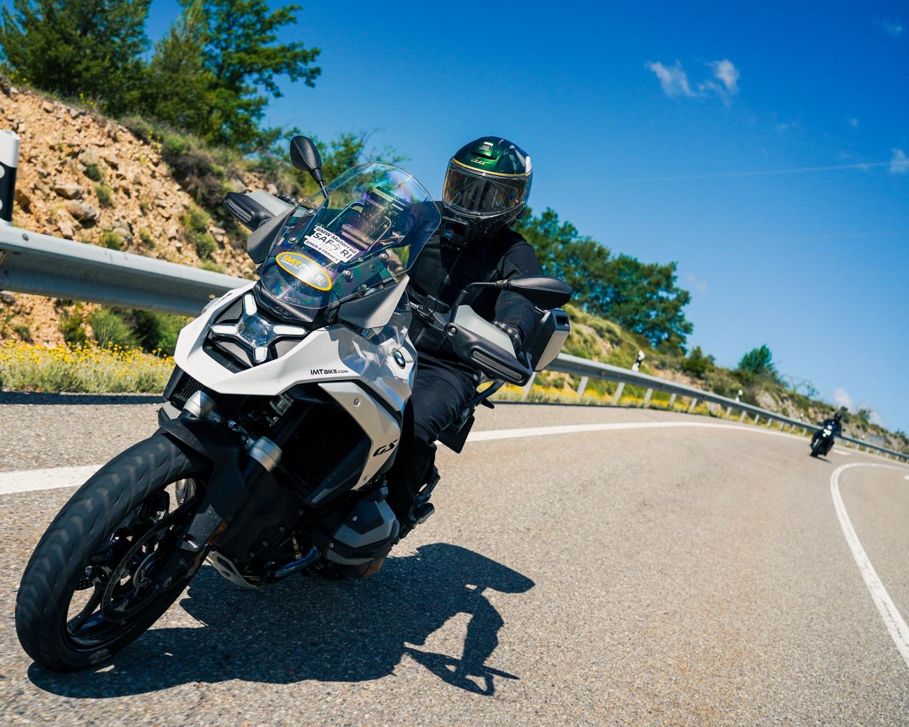 BMW GS adventure motorcycle leaning into a sun-drenched curve on a Spanish hillside road.