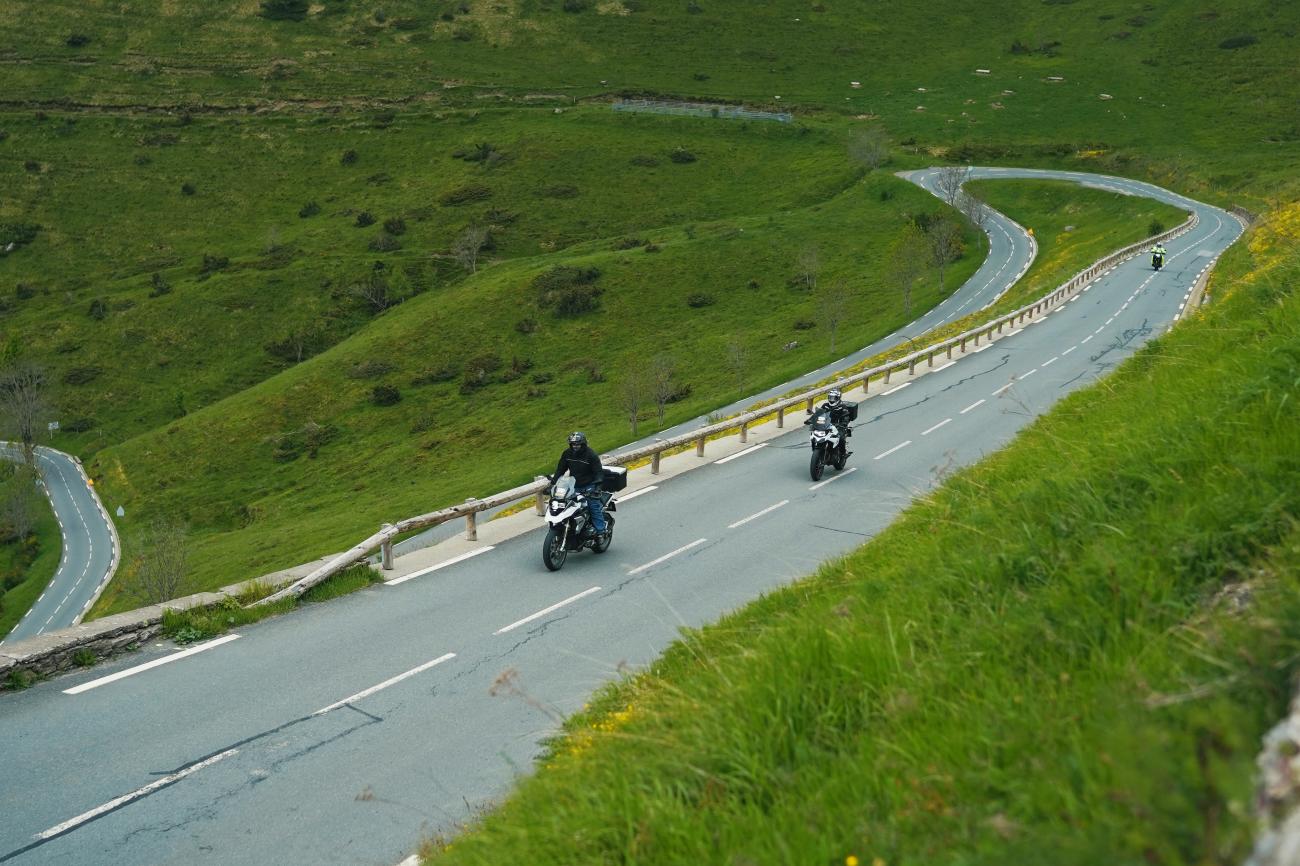 Motorcyclists riding through lush green switchback roads on a French Pyrenees mountain pass.