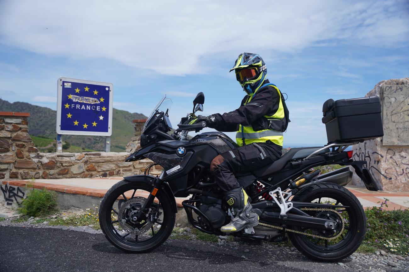 Motorcyclist on a BMW GS posing next to the France border sign at a Pyrenees mountain crossing.