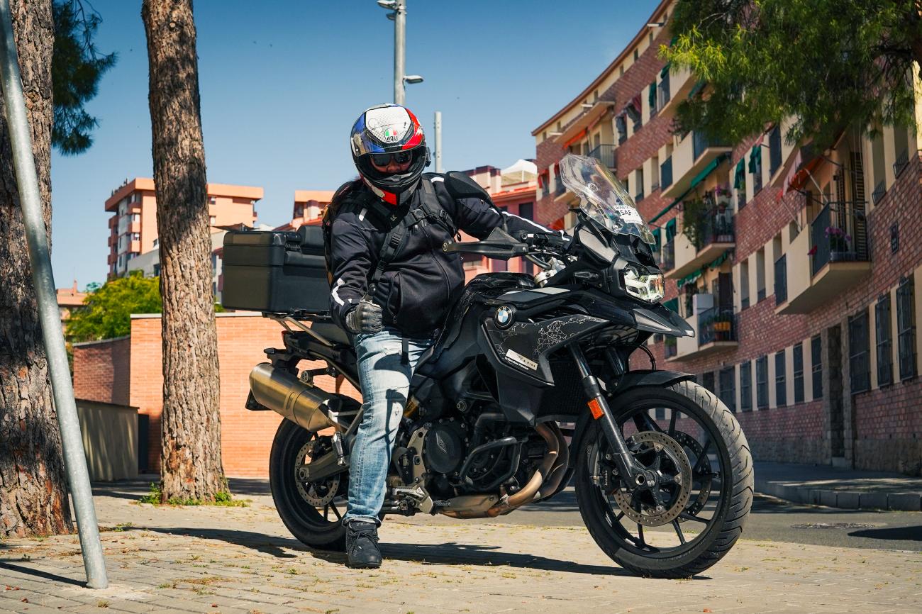 Motorcyclist seated on a BMW F 750 GS parked on a tree-lined street in Barcelona.