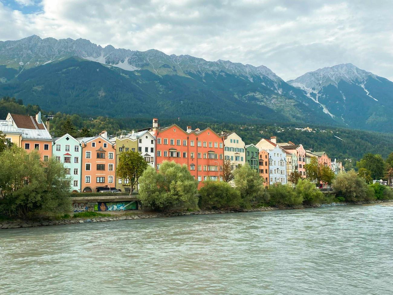 Colorful waterfront houses along the Inn River in Innsbruck with the Austrian Alps rising behind them.