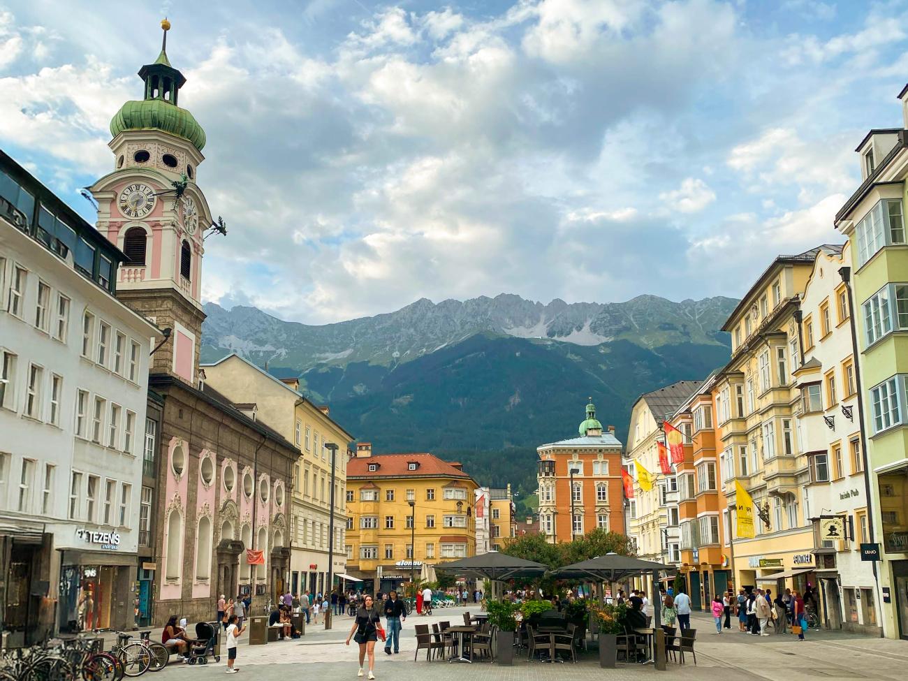 Historic old town square in Innsbruck with a clock tower and the Nordkette mountain range in the background.